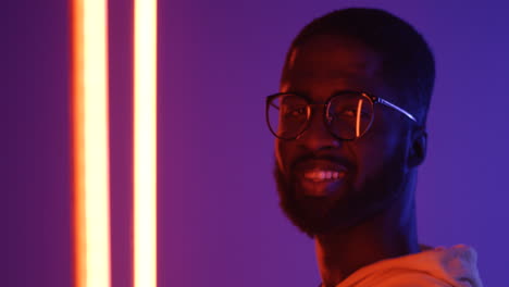 Close-upof-teh-profile-of-the-young-African-American-man-in-glasses-turning-his-head-to-the-camera-and-smiling.-Portrait.-Neon-lights.